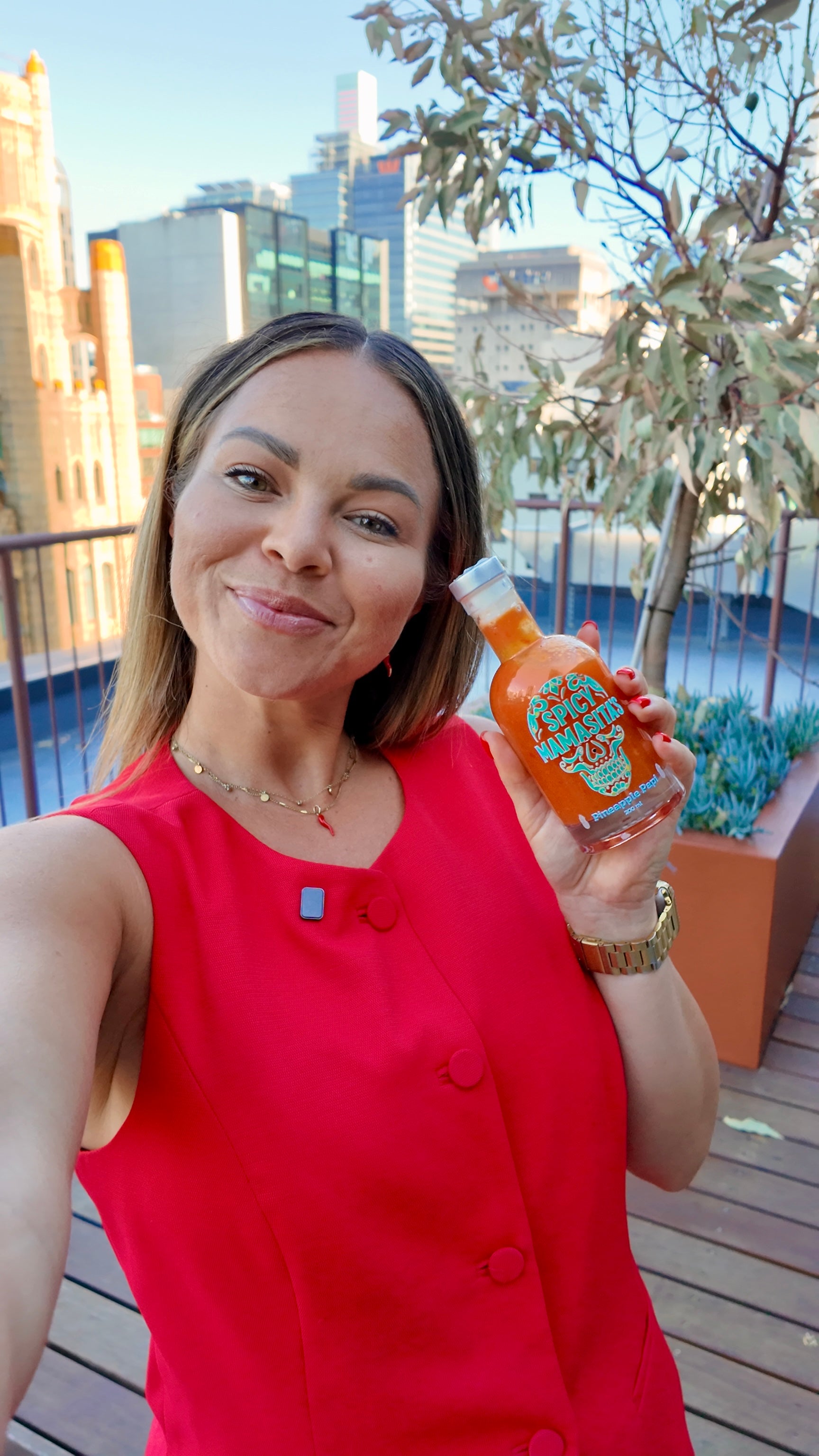 Woman in a red dress holding a bottle of hot sauce on a rooftop with cityscape background